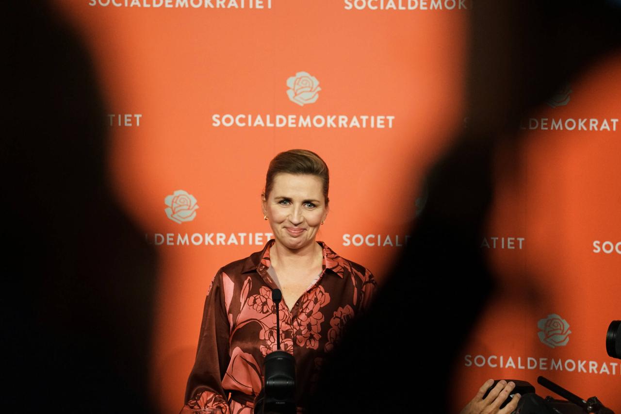 Eine Frau mit hochgestecktem Haar wird fotografiert vor einer orangenen Wahlwerbe-Wand auf der "Sozialdemokratie" steht. Eine Frau mit hochgestecktem Haar wird fotografiert vor einer orangenen Wahlwerbe-Wand auf der "Sozialdemokratie" steht.