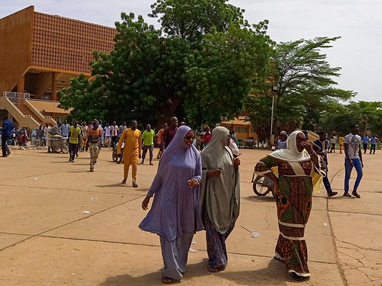 Einige Frauen aus Niger sind im Vordergrund zu sehen, im Hintergrund zahlreiche Passanten vor einem Fußballstadion