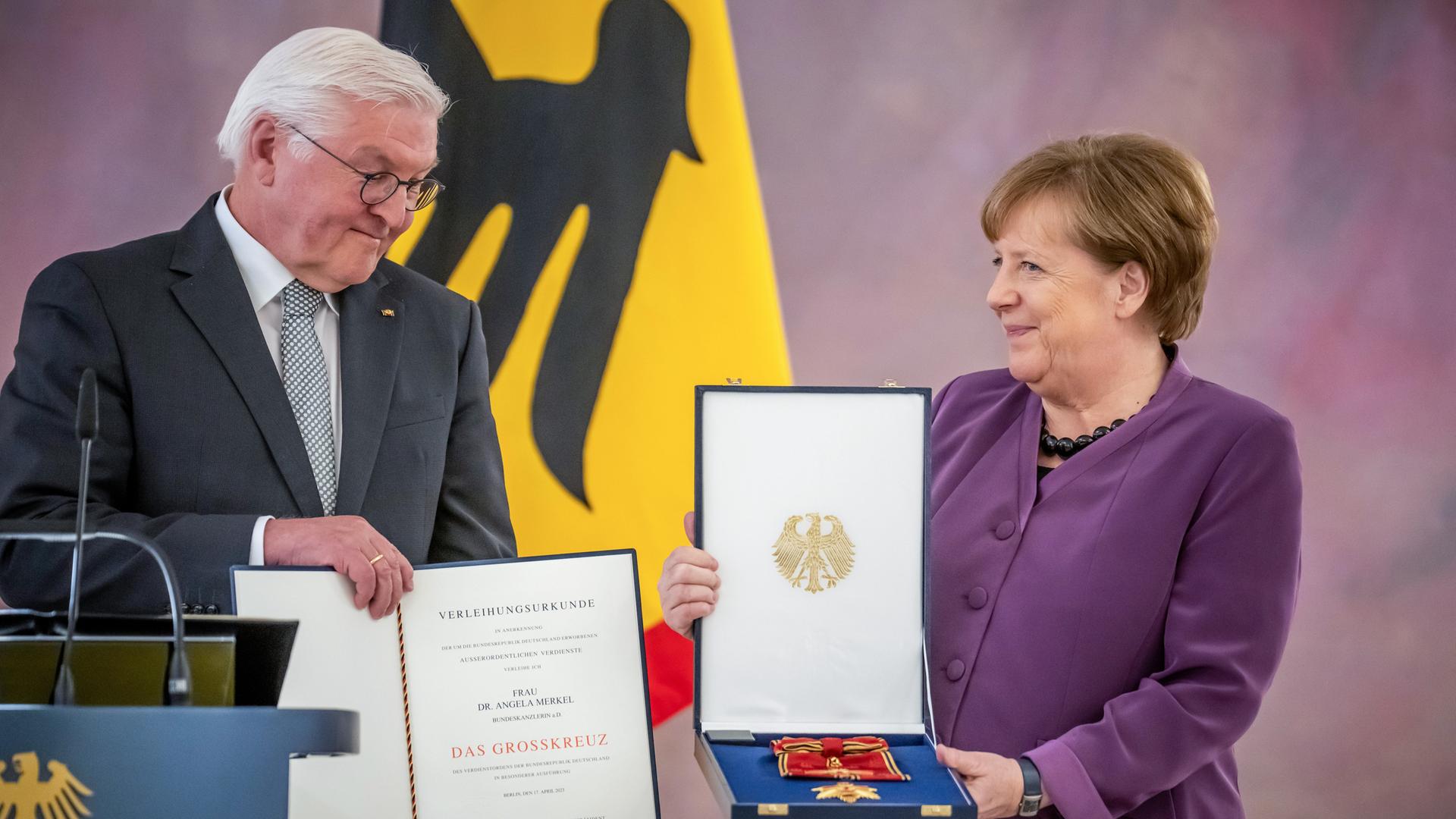Bundes-Präsident Steinmeier und die früheren Bundes-Kanzlerin Angela Merkel. Er überreicht ihr das Groß-Kreuz.