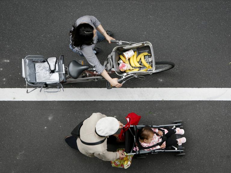 Eine Frau mit Einkäufen im Fahrradkorb aus der Vogelperspektive.