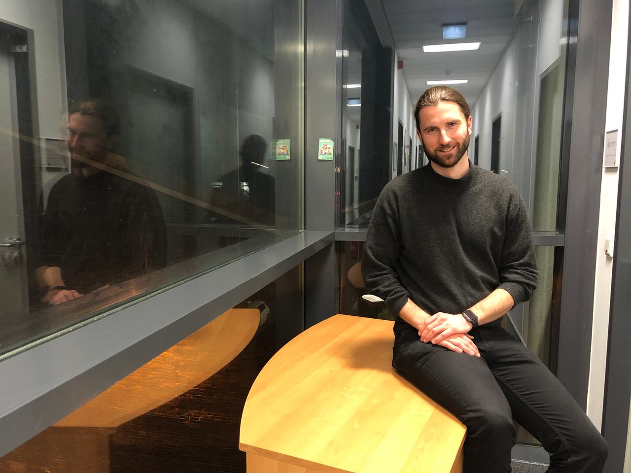 Ein junger Mann in Pullover und schwarzer Jeans sitzt auf einem Tisch. Ein junger Mann in Pullover und schwarzer Jeans sitzt auf einem Tisch.