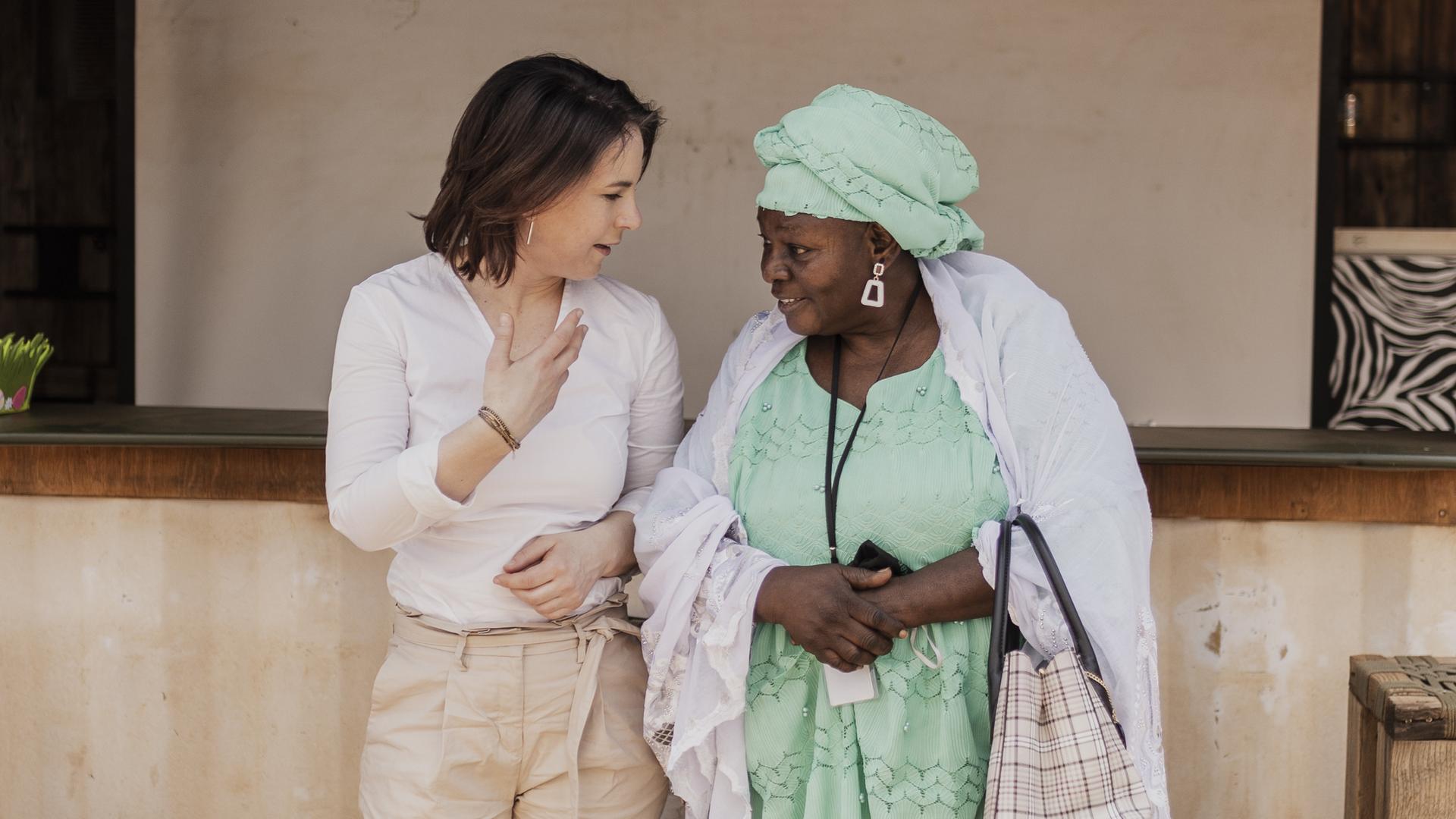 Die Bundesaussenministerin Annalena Bearbock steht mit einer Frau in traditioneller Tracht vor einer Hauswand, Mali 2022. Die Bundesaussenministerin Annalena Bearbock steht mit einer Frau in traditioneller Tracht vor einer Hauswand, Mali 2022.