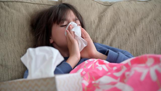 Ein Mädchen sitzt auf dem Sofa und schnäuzt sich die Nase. Wegen zunehmender Fälle von Infektionen mit dem Respiratorischen Synzytial-Virus (RSV) bei Kindern spitzt sich die Lage in vielen Kliniken zu