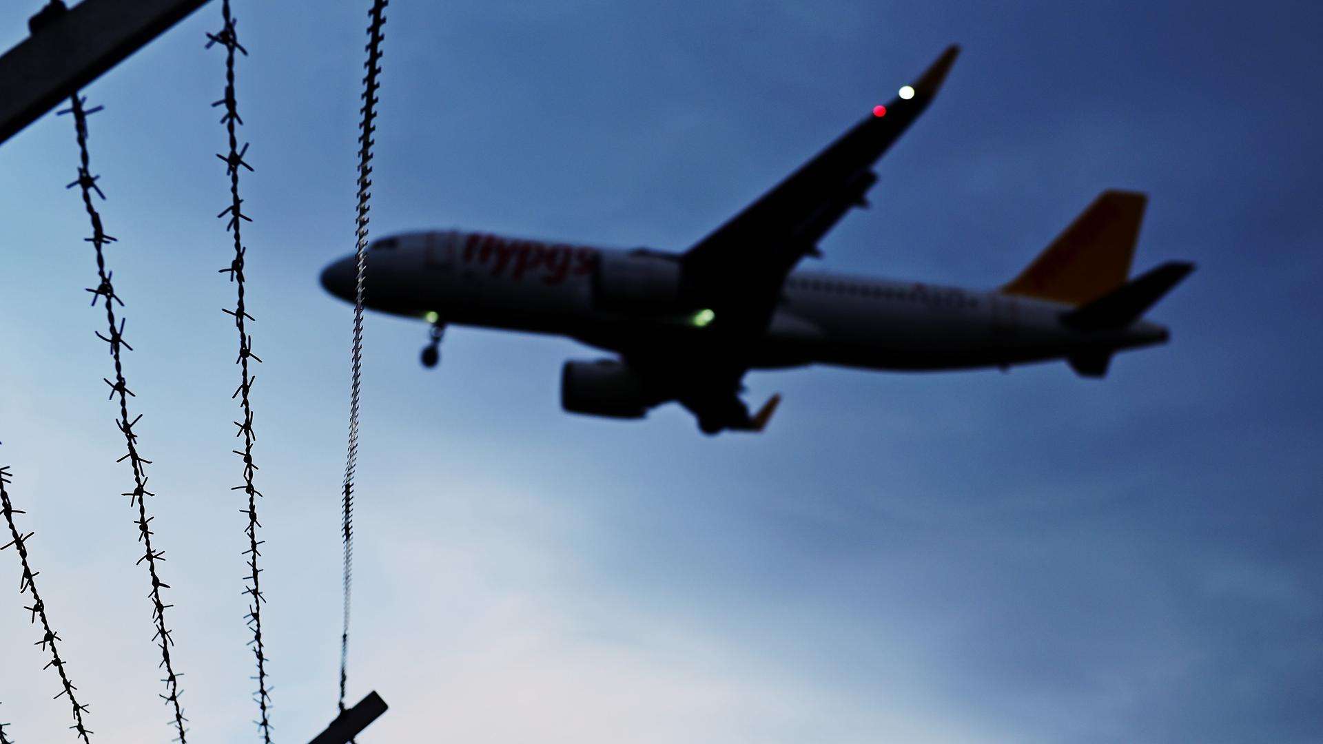 Ein Flugzeug fliegt vor nachtblauem Himmel über einen Gitterdrahtzaun Ein Flugzeug fliegt vor nachtblauem Himmel über einen Gitterdrahtzaun