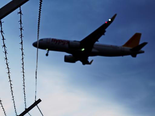 Ein Flugzeug fliegt vor nachtblauem Himmel über einen Gitterdrahtzaun