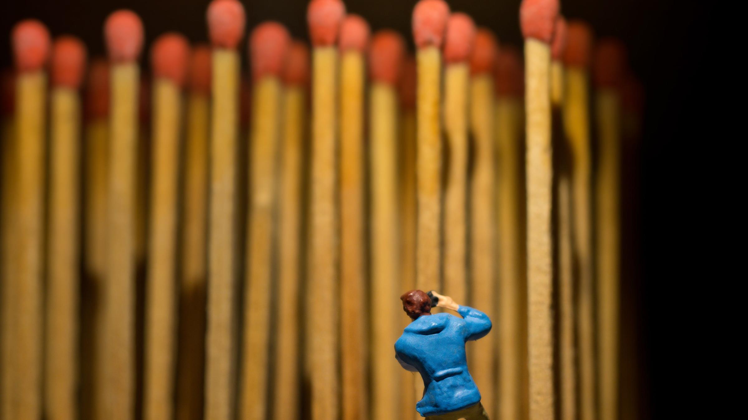 Eine Miniatur-Figur steht vor einer Reihe aufrecht stehender Streichhölzer mit roten Zündkopf.