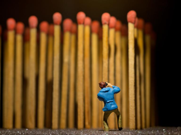 Eine Miniatur-Figur steht vor einer Reihe aufrecht stehender Streichhölzer mit roten Zündkopf.