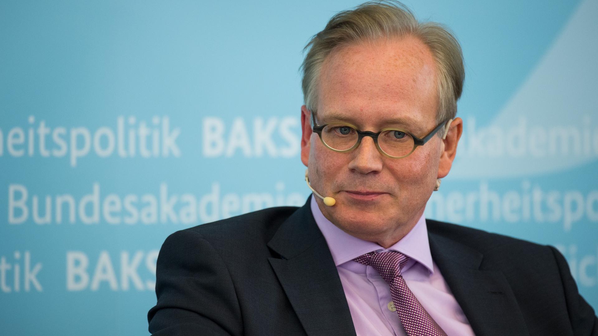 Ein mittelalter Mann mit hoher Stirn und runder Hornbrille sitzt im dunklen Anzug mit einem Mirkofon um die Ohren vor einer hellblauen Wand mit dem Schriftzug "BAKS Bundesakademie für Sicherheitspolitik" Ein mittelalter Mann mit hoher Stirn und runder Hornbrille sitzt im dunklen Anzug mit einem Mirkofon um die Ohren vor einer hellblauen Wand mit dem Schriftzug "BAKS Bundesakademie für Sicherheitspolitik"