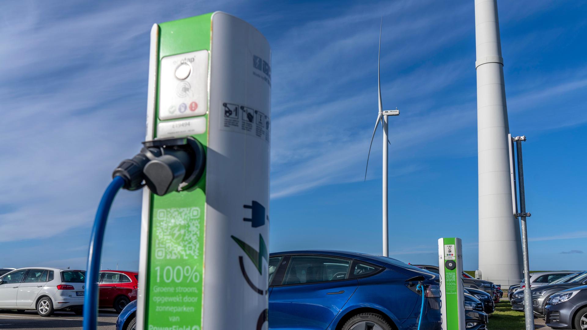 E-Auto Schnellladestation vor blauem Himmel, Windräder im Hintergrund E-Auto Schnellladestation vor blauem Himmel, Windräder im Hintergrund