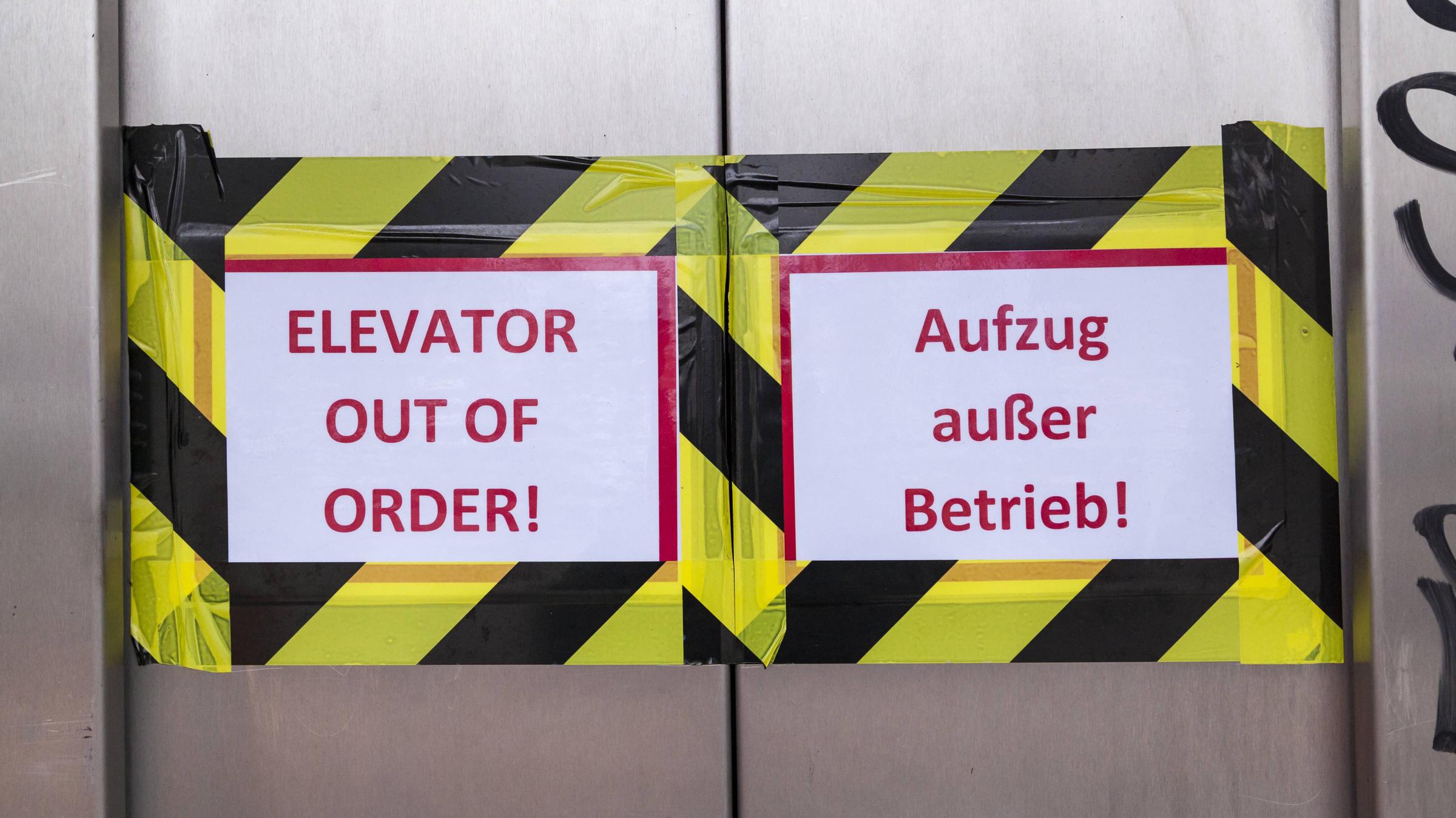 Blick auf die geschlossenen Türen eines Berliner Fahrstuhls, links ein mit Klebeband befestigtes Schild mit der Aufschrift "Elevator out of order!", rechts "Fahrstuhl außer Betrieb!"