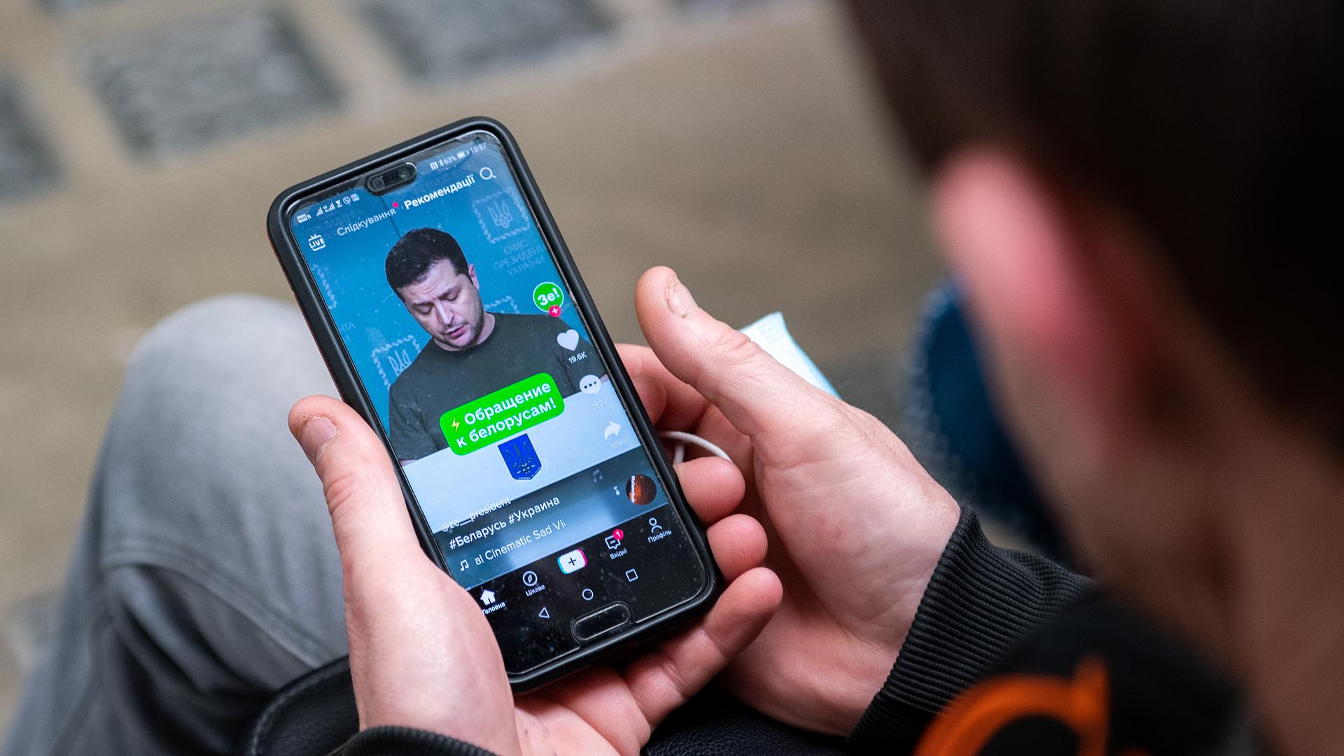 Ein ukrainischer Flüchtling hält ein Smartphone in der Hand und sieht sich das Video einer Rede von Wolodymr Selenskyi an. Ein ukrainischer Flüchtling hält ein Smartphone in der Hand und sieht sich das Video einer Rede von Wolodymr Selenskyi an.