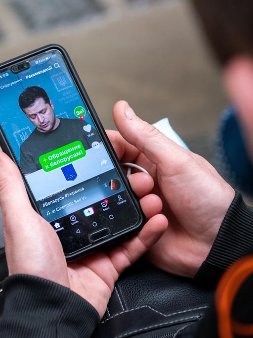 Ein ukrainischer Flüchtling hält ein Smartphone in der Hand und sieht sich das Video einer Rede von Wolodymr Selenskyi an.