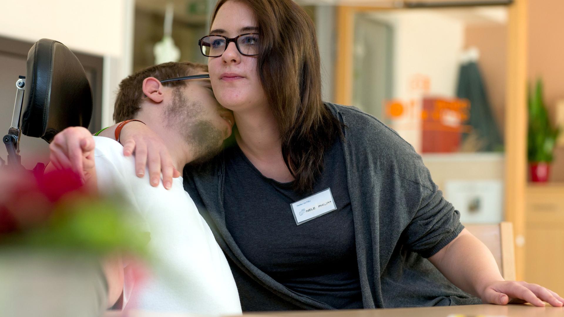 Freiwilliges Soziales Jahr: Eine junge Frau kümmert sich in einem Wohnheim der Diakonie um einen behinderten jungen Mann. Dieser legt vertrauensvoll sein Gesicht an ihre Schulter. Freiwilliges Soziales Jahr: Eine junge Frau kümmert sich in einem Wohnheim der Diakonie um einen behinderten jungen Mann. Dieser legt vertrauensvoll sein Gesicht an ihre Schulter.