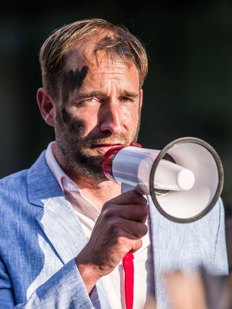 Der Aktionskünstler Philipp Ruch steht mit schwarz angemaltem Gesicht auf einer Straße und hält ein Megafon vor das Gesicht.