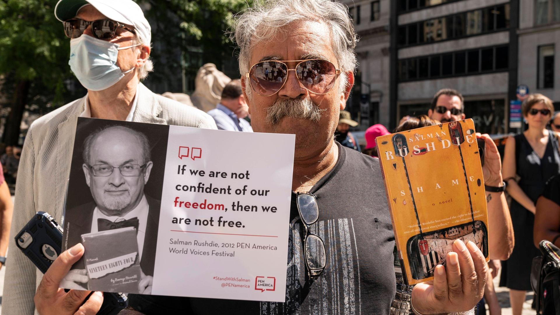Ein Aktivist hält im August 2022 in New York während der PEN America-Kundgebung zur Unterstützung von Salman Rushdie ein Plakat mit einem Bild von Salman Rushdie und dem Zitat "If we are not confident of our freedom, then we are not free." sowie ein Buch von Rushdie. Ein Aktivist hält im August 2022 in New York während der PEN America-Kundgebung zur Unterstützung von Salman Rushdie ein Plakat mit einem Bild von Salman Rushdie und dem Zitat "If we are not confident of our freedom, then we are not free." sowie ein Buch von Rushdie.