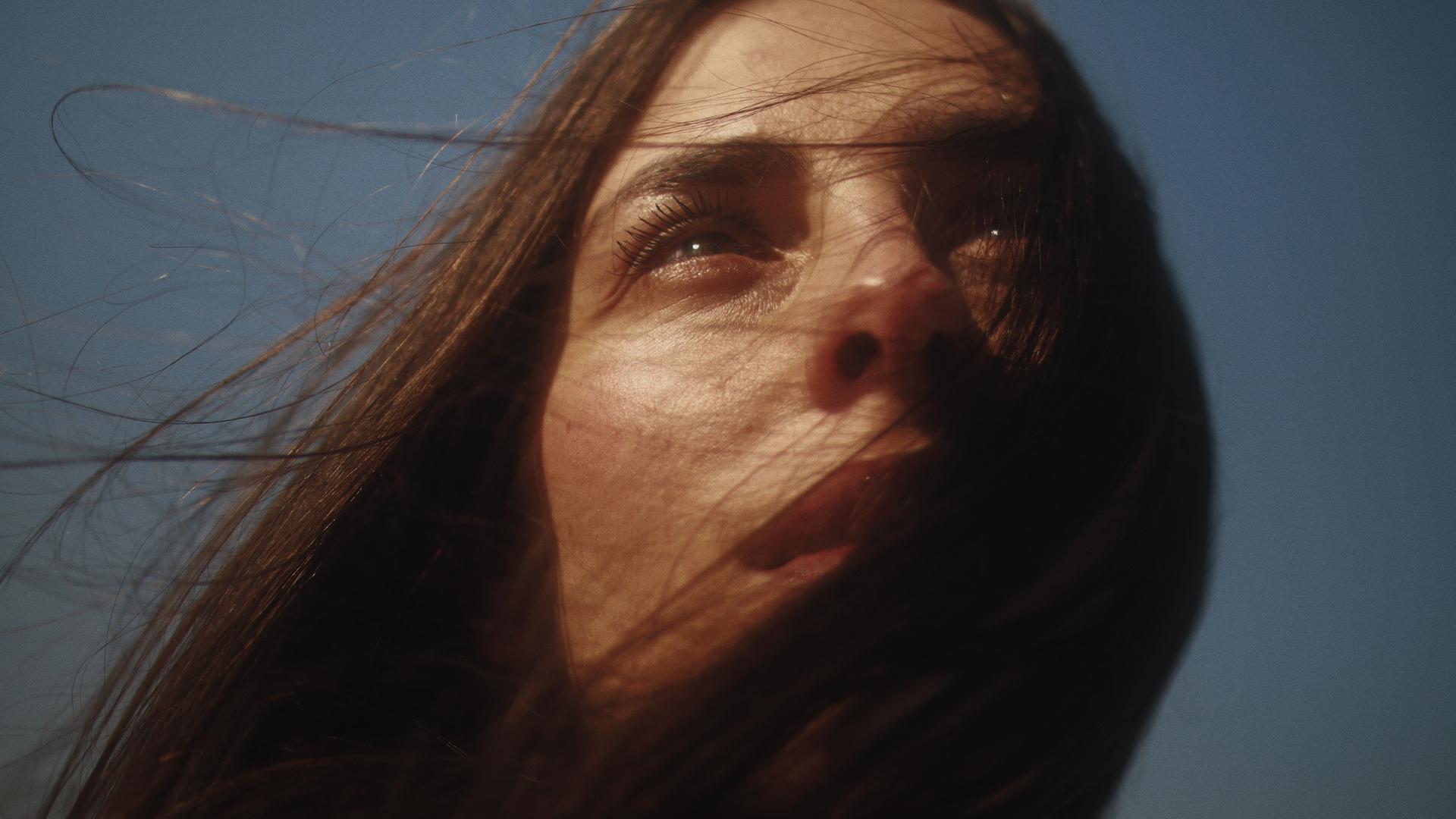 Einer jungen Frau wehen die braunen Haare ins Gesicht und sie schaut in den Himmel. Einer jungen Frau wehen die braunen Haare ins Gesicht und sie schaut in den Himmel.