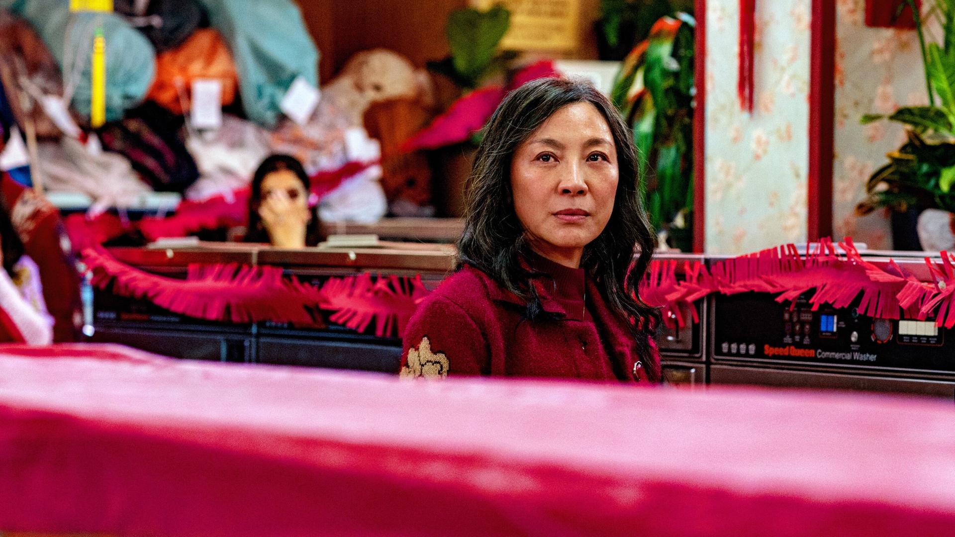 Michelle Yeoh blickt ernst über die Kante eines roten Sofas Michelle Yeoh blickt ernst über die Kante eines roten Sofas