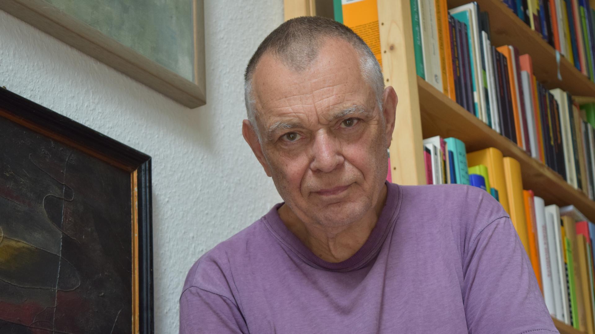 Der Komponist Mathias Spahlinger sitzt auf einer Treppe vor Bücherregalen und schaut in die Kamera Der Komponist Mathias Spahlinger sitzt auf einer Treppe vor Bücherregalen und schaut in die Kamera