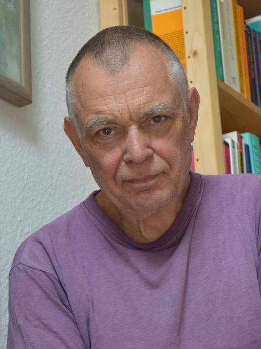 Der Komponist Mathias Spahlinger sitzt auf einer Treppe vor Bücherregalen und schaut in die Kamera