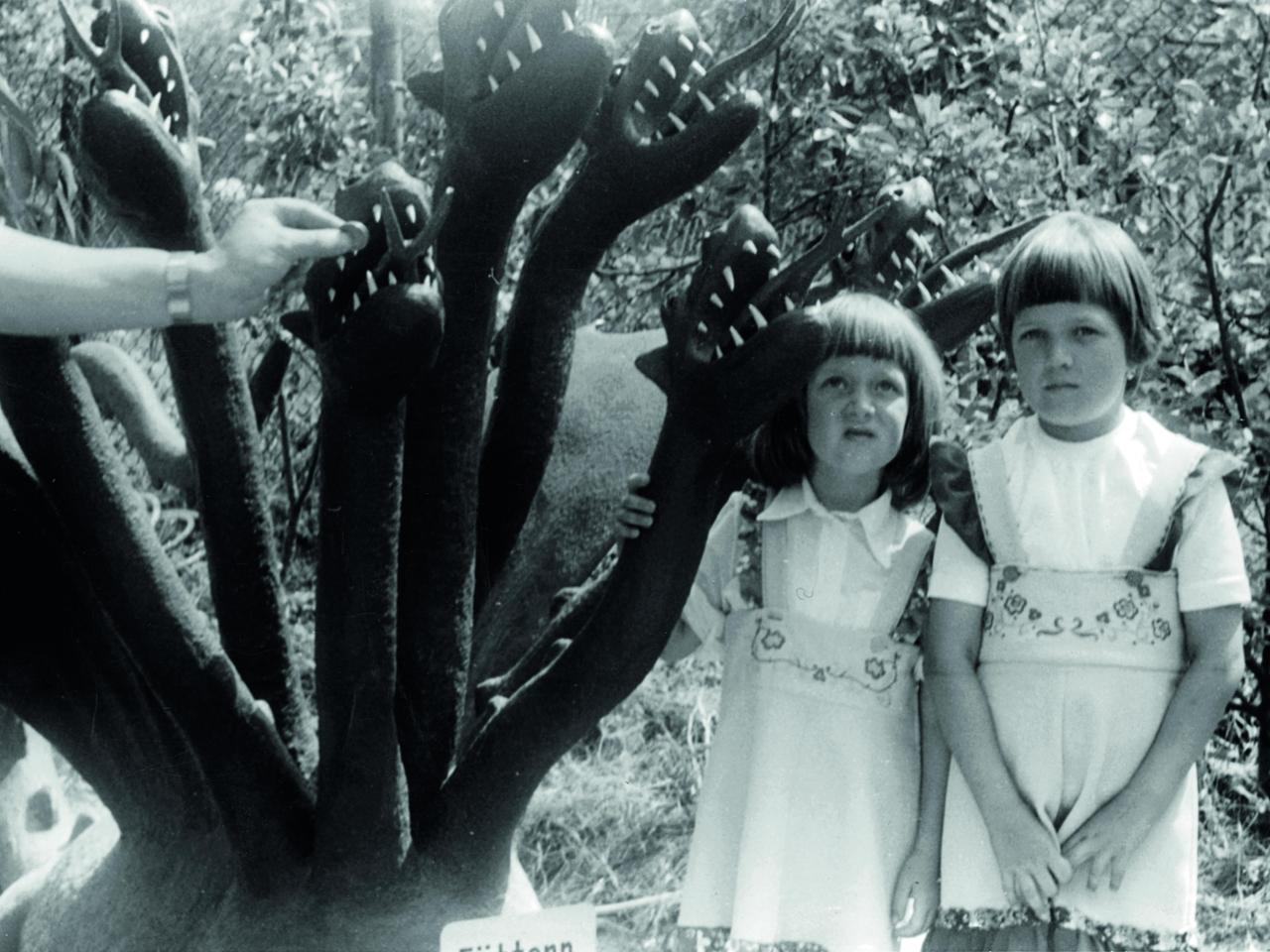 Zwei kleine Mädchen posieren neben dem Modell eines mehrköpfigen Monsters.