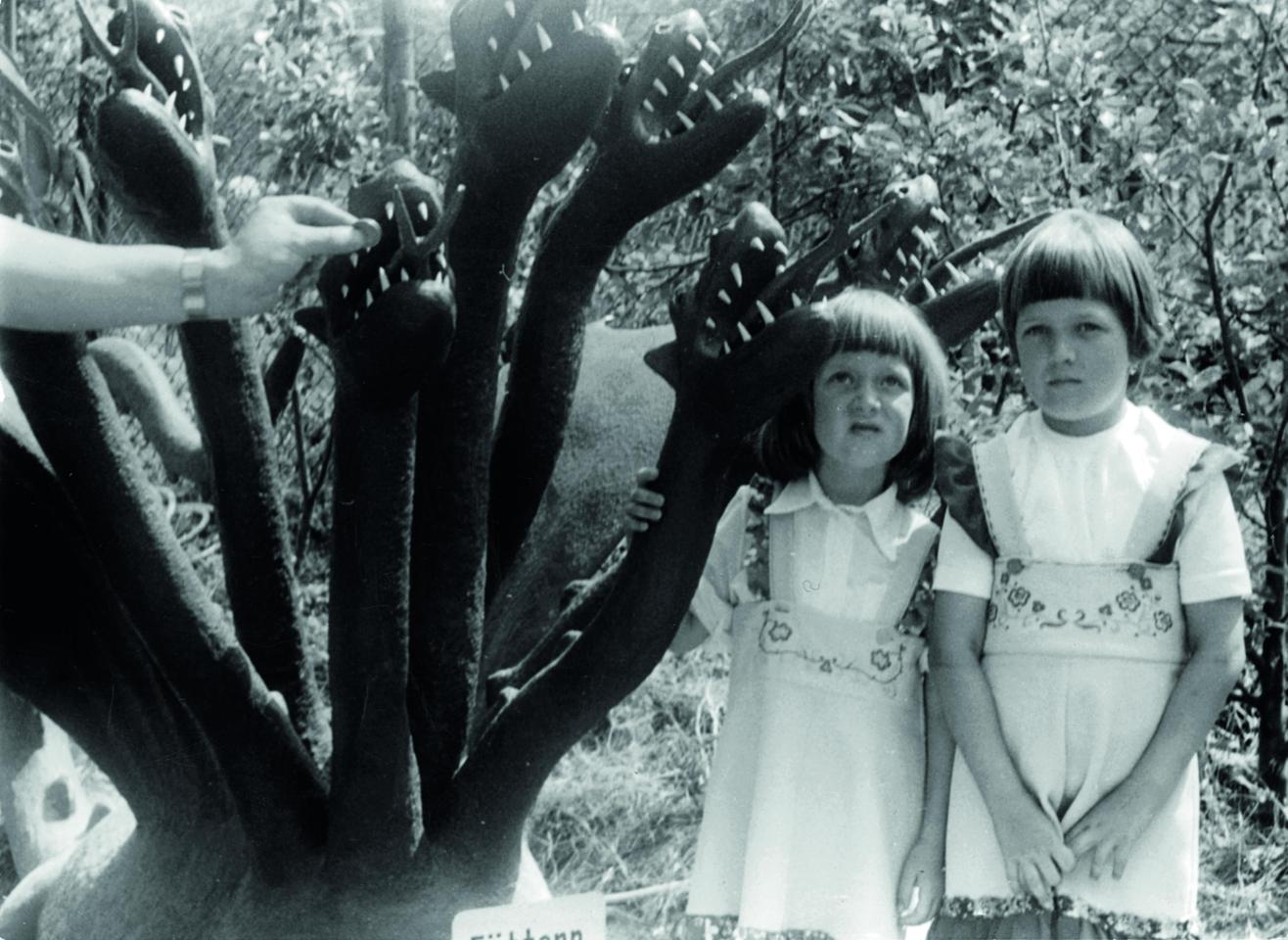 Zwei kleine Mädchen posieren neben dem Modell eines mehrköpfigen Monsters.