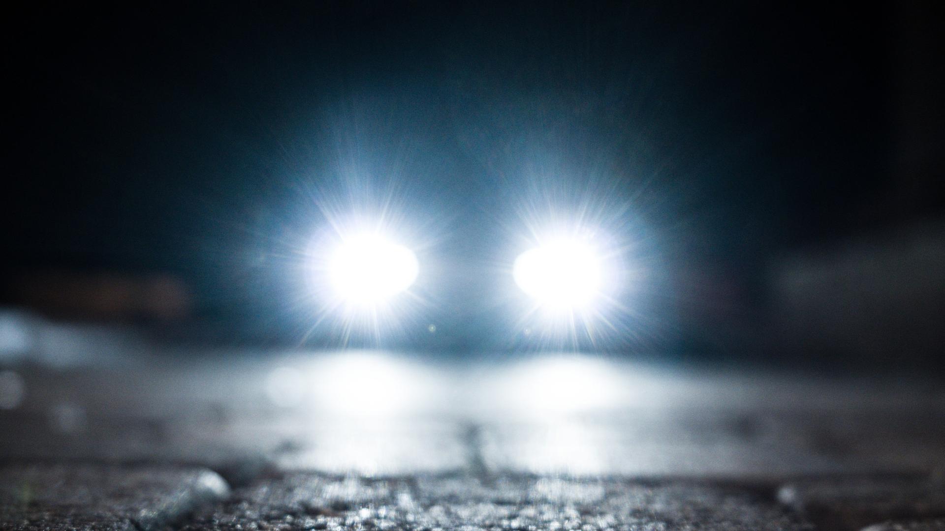 Kopfsteinpflaster in der Dunkelheit. Ein Auto nähert sich mit blendendgrellen Scheinwerfern.