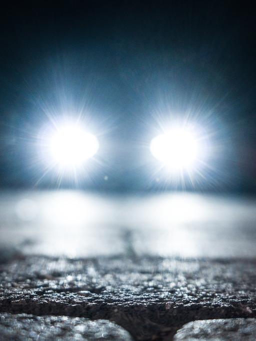 Kopfsteinpflaster in der Dunkelheit. Ein Auto nähert sich mit blendendgrellen Scheinwerfern.