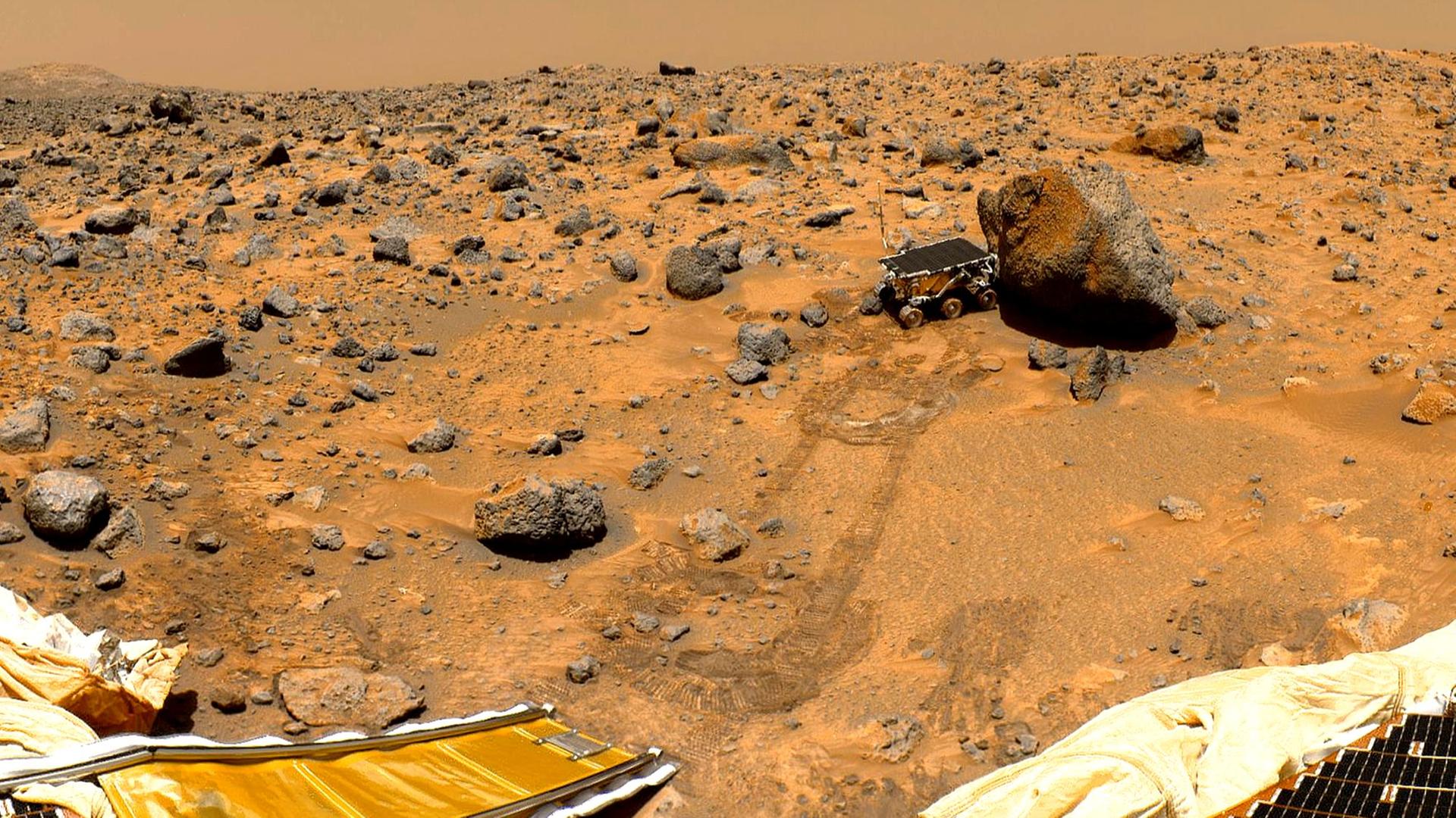 Der kleine Rover Sojourner im Sommer 1997 beim Betrachten eines Steins auf dem Mars Der kleine Rover Sojourner im Sommer 1997 beim Betrachten eines Steins auf dem Mars