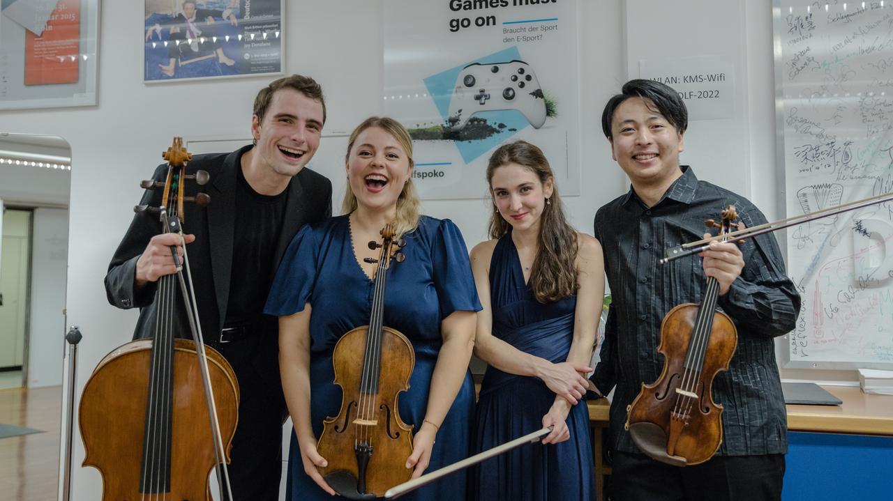 Ein Cellist, eine Bratschistin, eine Pianistin und ein Geiger posieren lachend vor einer Wand im Künstlerbereich des Dlf Kammermusiksaals. Ein Cellist, eine Bratschistin, eine Pianistin und ein Geiger posieren lachend vor einer Wand im Künstlerbereich des Dlf Kammermusiksaals.