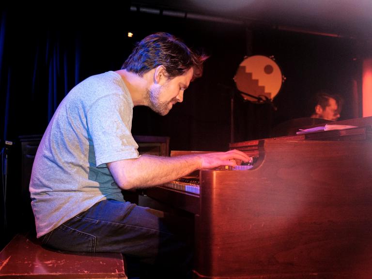 Kit Downes sitzt im grauen Shirt vertieft über einer Hammond-Orgel und spielt mit geschlossenen Augen auf einer Clubbühne.