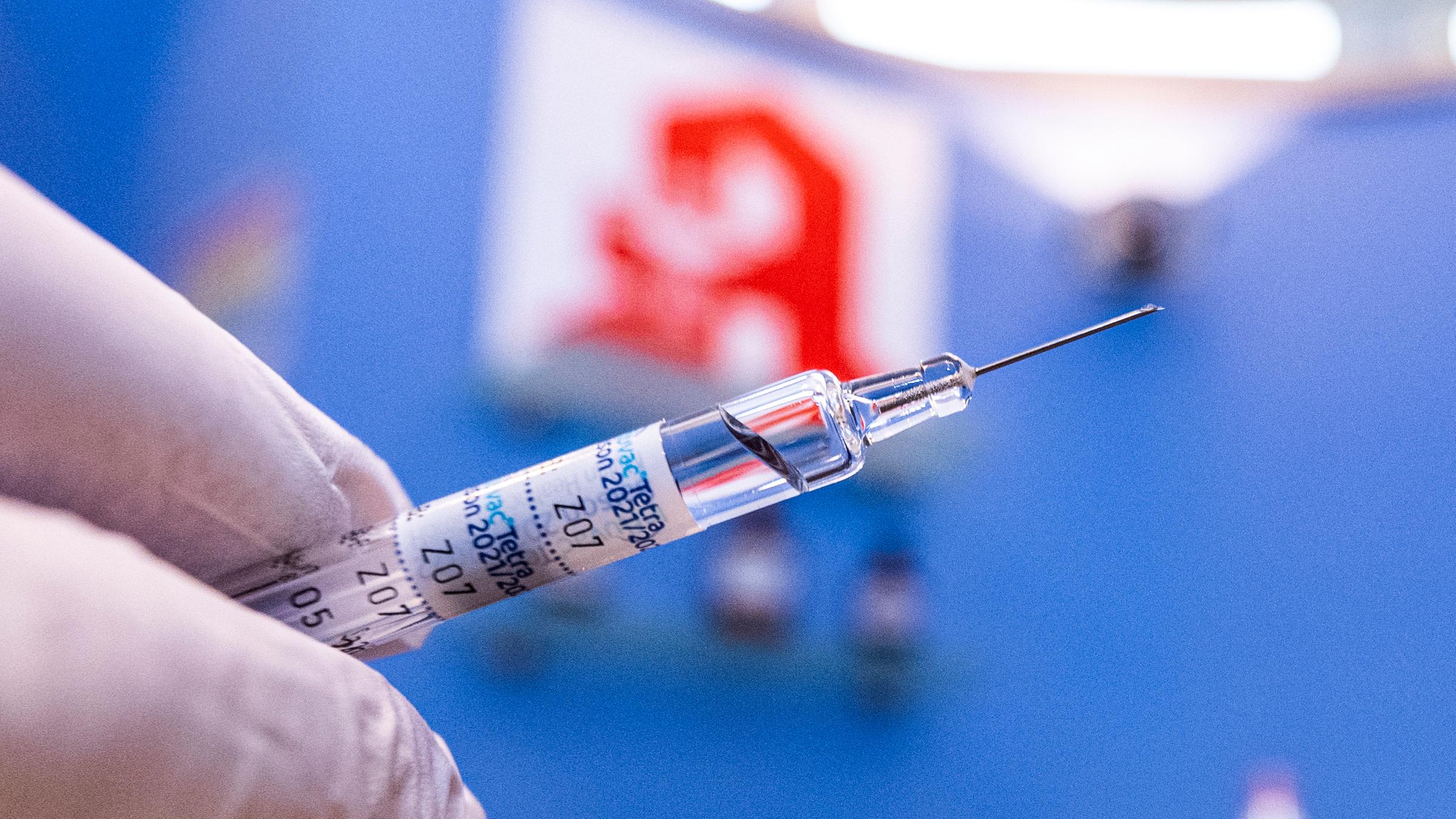 Apotheker Michael Beckmann hält eine Spritze mit Grippeschutzimpfstoff vor dem Apotheke-Logo. 