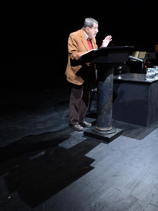 Der Schriftsteller Günter Grass steht auf einer Bühne vor einem Stehpult und liest aus einem Buch vor. 