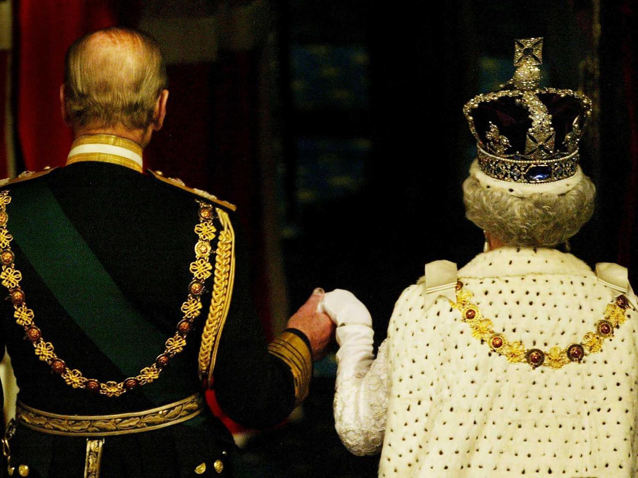 Queen Elizabeth II. und Prinz Philip sind von hinten zu sehen, während sie das House of Lords verlassen. Sie trägt Krone und Hermelinmantel.