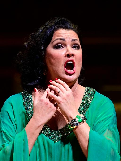 Auf dem Bild ist die Operndiva Anna Netrebko zu sehen. Sie trägt ein türkises Abendkleid und singt voller Inbrust. 