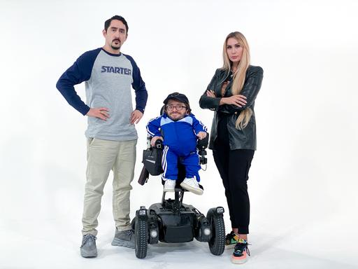 Eko Fresh und Sarah Bora stehen rechts und links neben Raul Krauthausen, der im Rollstuhl sitzt.