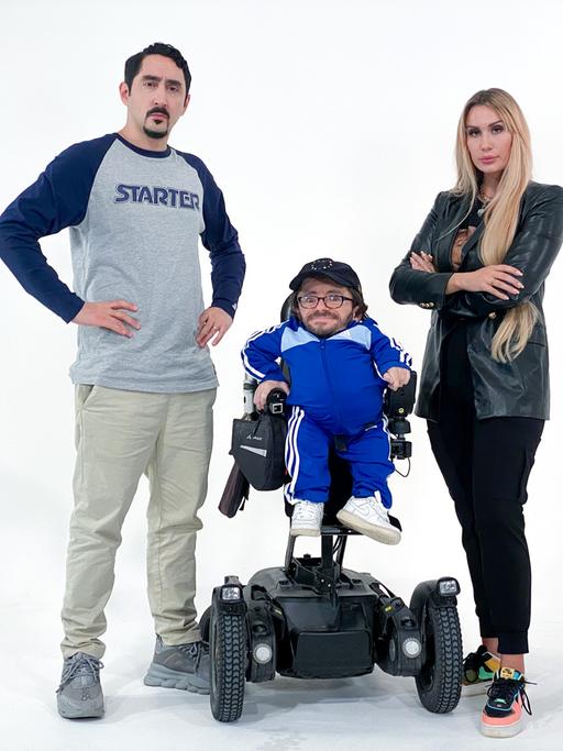 Eko Fresh und Sarah Bora stehen rechts und links neben Raul Krauthausen, der im Rollstuhl sitzt.