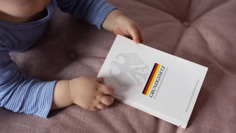 Ein Kleinkind hält ein deutsches Grundgesetz in der Hand.