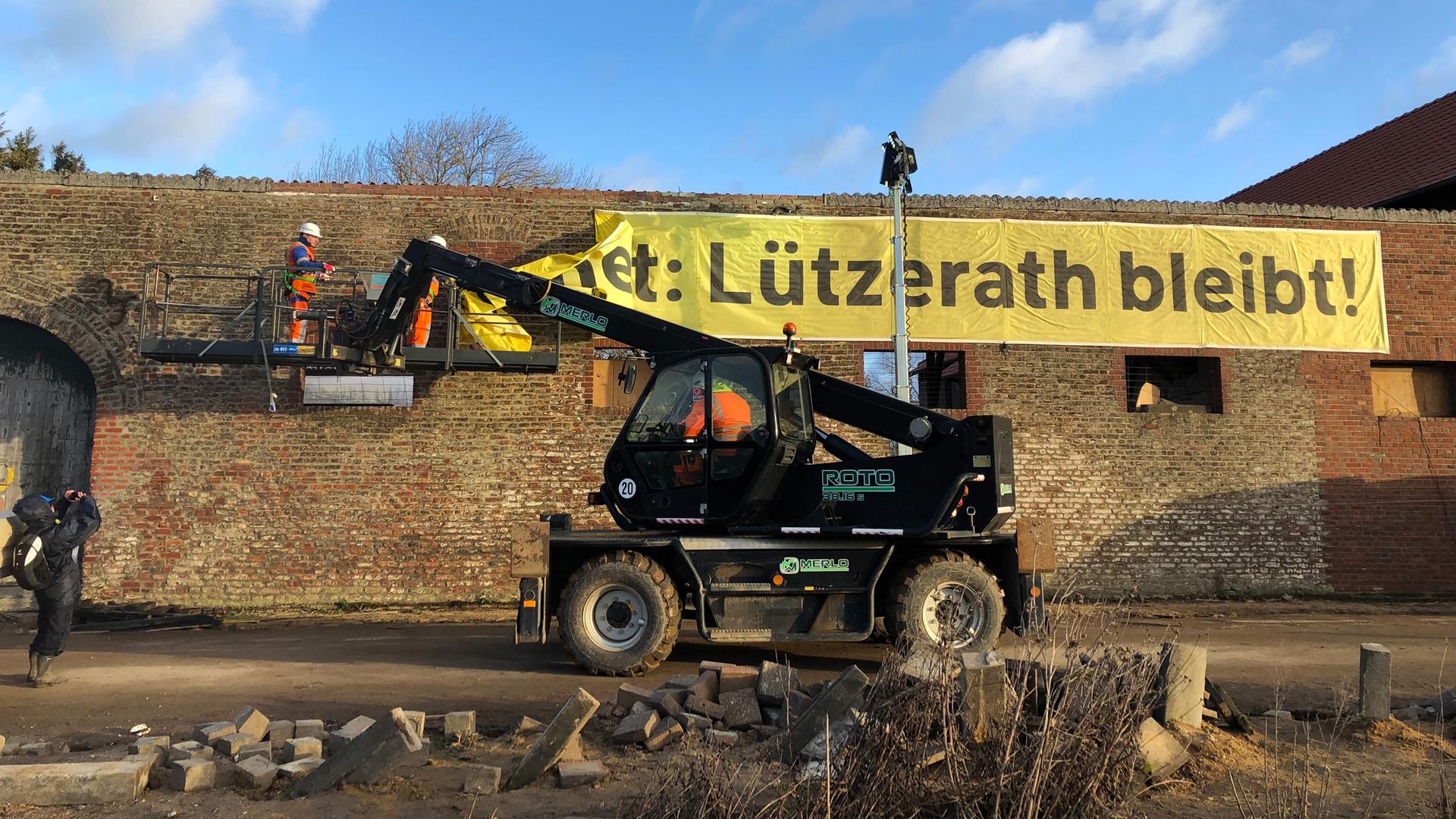 Arbeiter entfernen ein Banner "Lützerath bleibt!" von einer Wand. Arbeiter entfernen ein Banner "Lützerath bleibt!" von einer Wand.