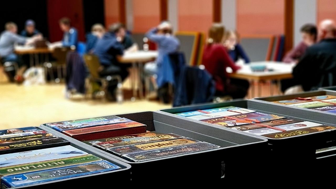 Im Vordergrund sind Spielkartenstapel zu sehen, während im Hintergrund an drei Tischen gespielt wird. Im Vordergrund sind Spielkartenstapel zu sehen, während im Hintergrund an drei Tischen gespielt wird.
