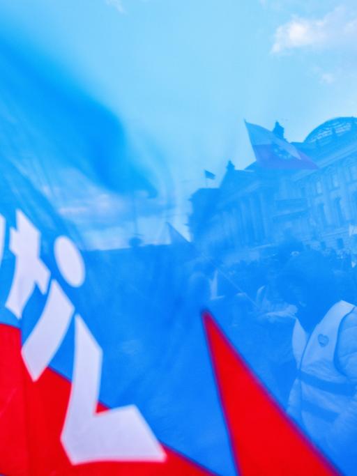 Demonstranten vor dem Berliner Reichstag sind durch den blauen Stoff einer AfD-Parteiflagge hindurch zu sehen.