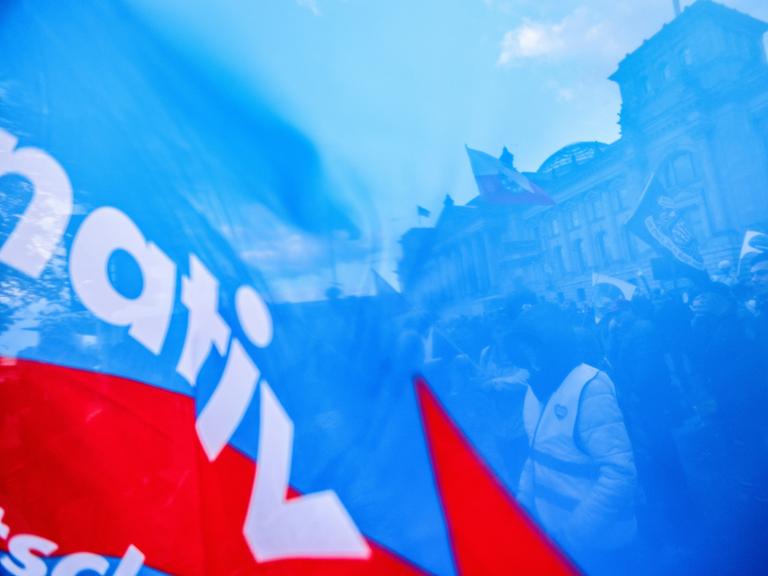 Demonstranten vor dem Berliner Reichstag sind durch den blauen Stoff einer AfD-Parteiflagge hindurch zu sehen.
