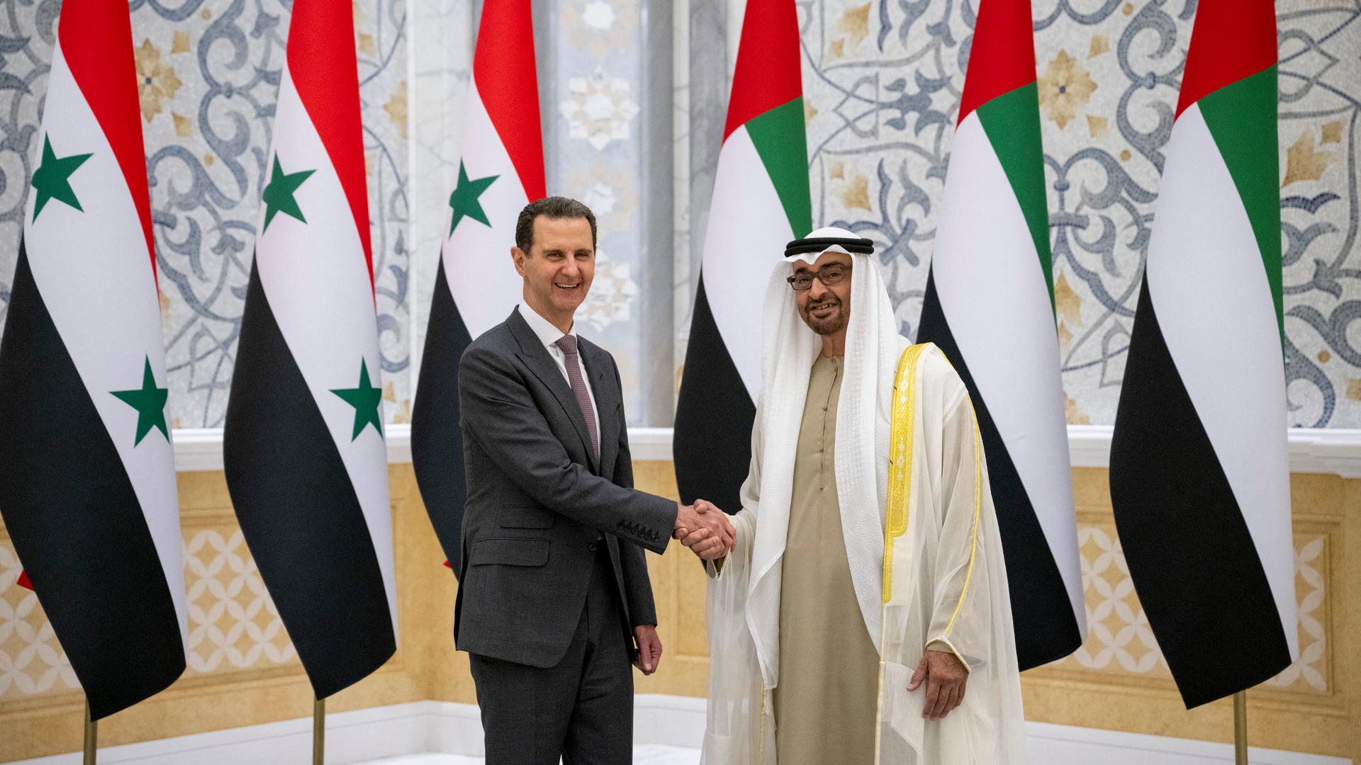 Der syrische Präsident Baschar al-Assad schüttelt dem Präsidenten der Vereinigten Arabischen Emirate, Scheich Mohammed bin Zayed, die Hand. Im Hintergrund sind Fahnen der beiden Länder.