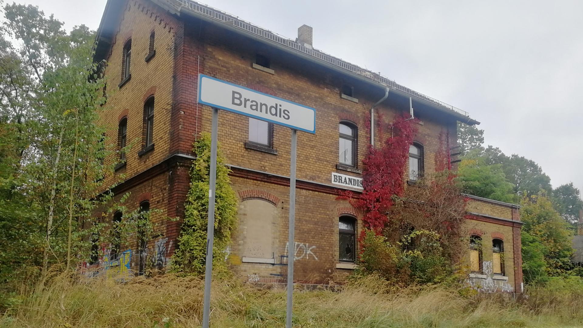 Das verfallene Bahnhofsgebäude von Brandis. Die Bahnsteige wachsen mit Gräsern zu. Vor dem Gebäude steht das Stationsschild "Brandis". Das verfallene Bahnhofsgebäude von Brandis. Die Bahnsteige wachsen mit Gräsern zu. Vor dem Gebäude steht das Stationsschild "Brandis".