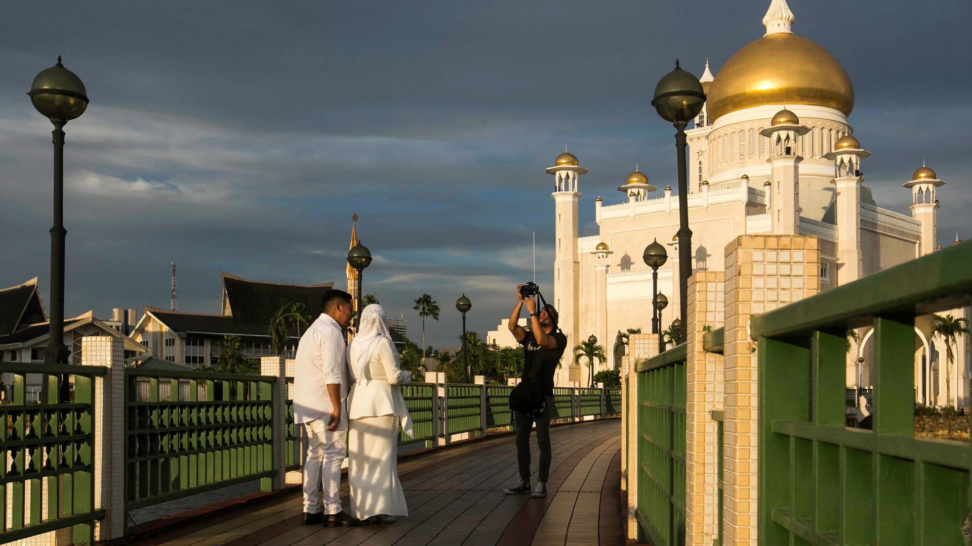 Ein frisch verheiratetes Paar lässt sich vor der Moschee Sultan Omar Ali Saifuddien in Brunei fotografieren, 2019. Ein frisch verheiratetes Paar lässt sich vor der Moschee Sultan Omar Ali Saifuddien in Brunei fotografieren, 2019.