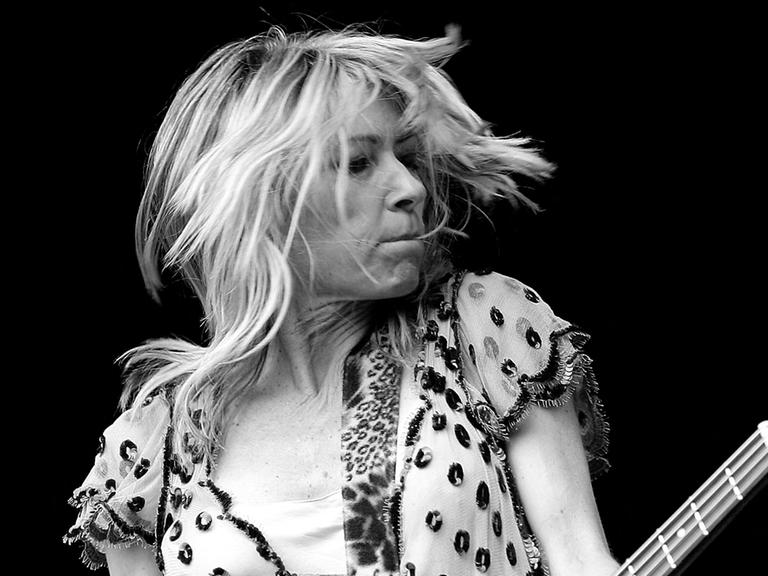 Die US-Musikerin Kim Gordon spielt auf der Bühne Bassgitarre. Sie trägt ein Kleid.