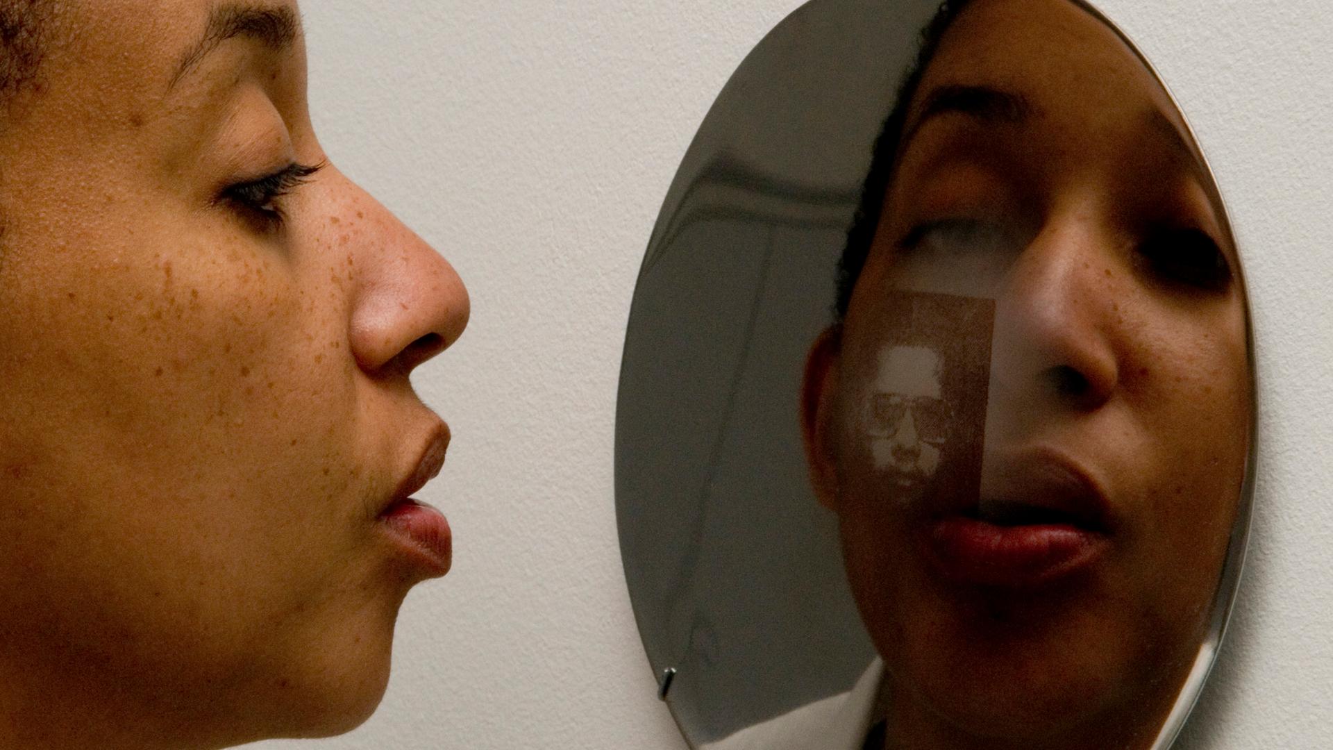 Eine Frau schaut in einen Spiegel, in dem man ihr Spiegelbild erkennt. Eine Frau schaut in einen Spiegel, in dem man ihr Spiegelbild erkennt.