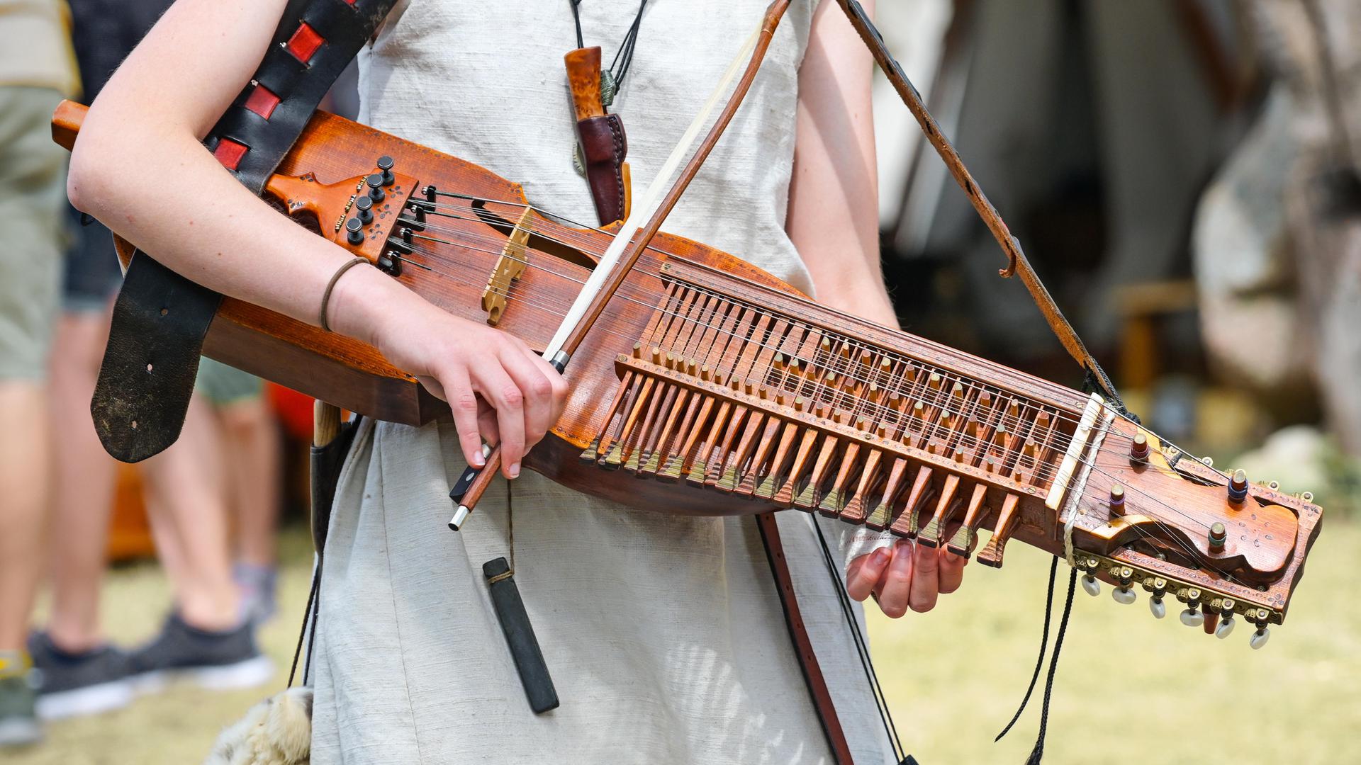 Eine junge Frau hat eine Nyckelharpa umgehangen und spielt diese mit einem kurzen Bogen. Eine junge Frau hat eine Nyckelharpa umgehangen und spielt diese mit einem kurzen Bogen.