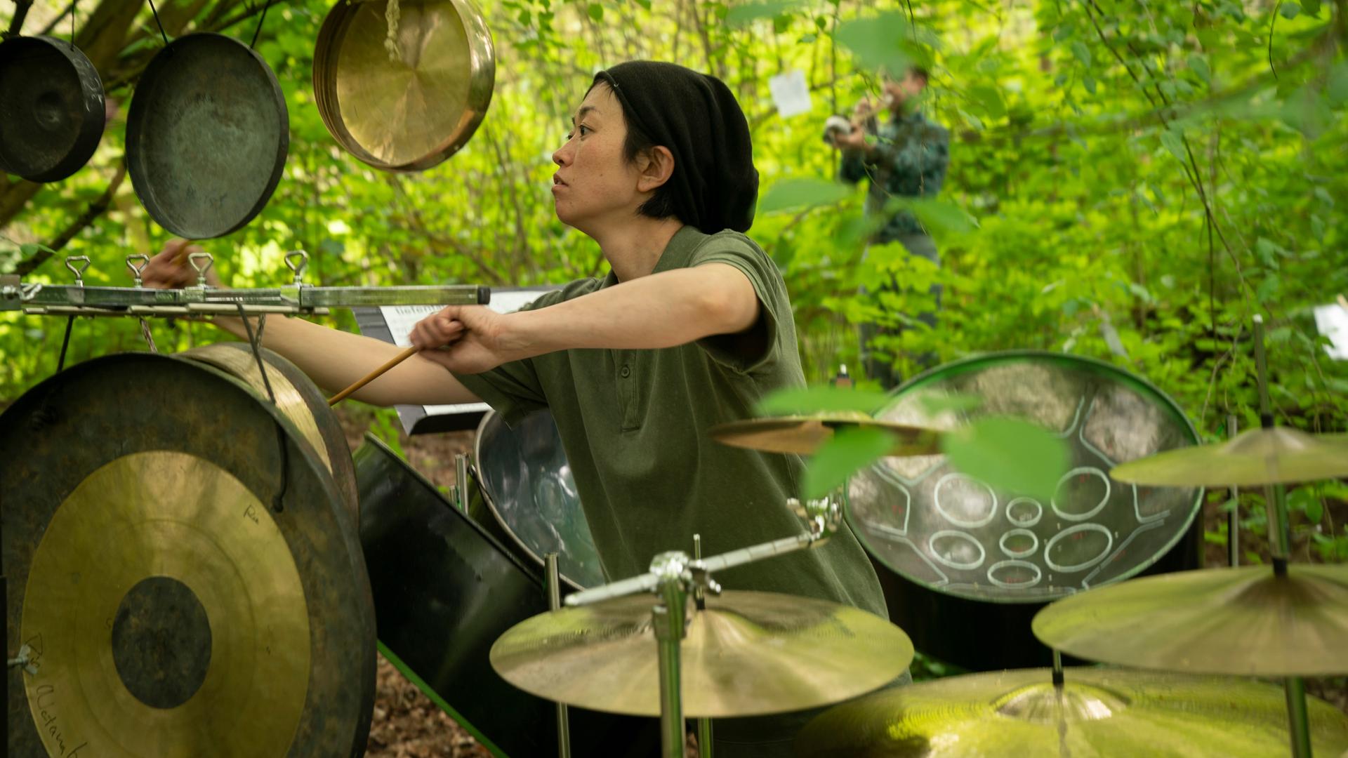 Marie Watanabe spielt unter einem günen Blätterdach Schlagzeug Marie Watanabe spielt unter einem günen Blätterdach Schlagzeug