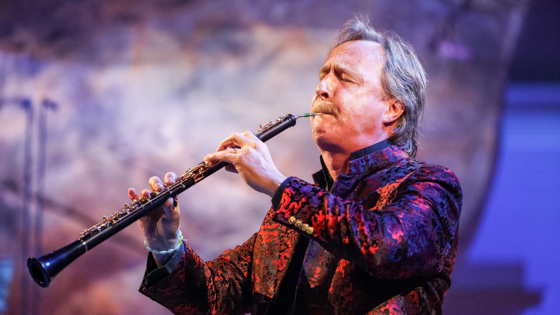 Ein Mann mit graumeliertem Haar spielt eine Oboe. Er trägt einen Oberlippenbart, sein Jackett erscheint in bunten Farben. Der Mann, Albrecht Mayer, ist im Profil zu sehen, er hat beim Spiel die Augen geschlossen. Ein Mann mit graumeliertem Haar spielt eine Oboe. Er trägt einen Oberlippenbart, sein Jackett erscheint in bunten Farben. Der Mann, Albrecht Mayer, ist im Profil zu sehen, er hat beim Spiel die Augen geschlossen.