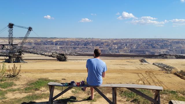 Mann sitzt auf einer Bank und schaut auf das Braunkohleabbaugebiet 